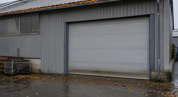 Industriehalle im Herbst mit laubgefüllter Dachrinne und geschlossenem Sektionaltor auf nassem Hof